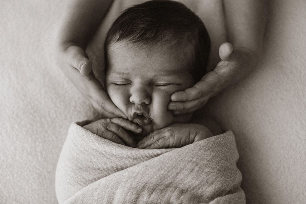 fotografia newborn y la mano de su hermano en los mofletes